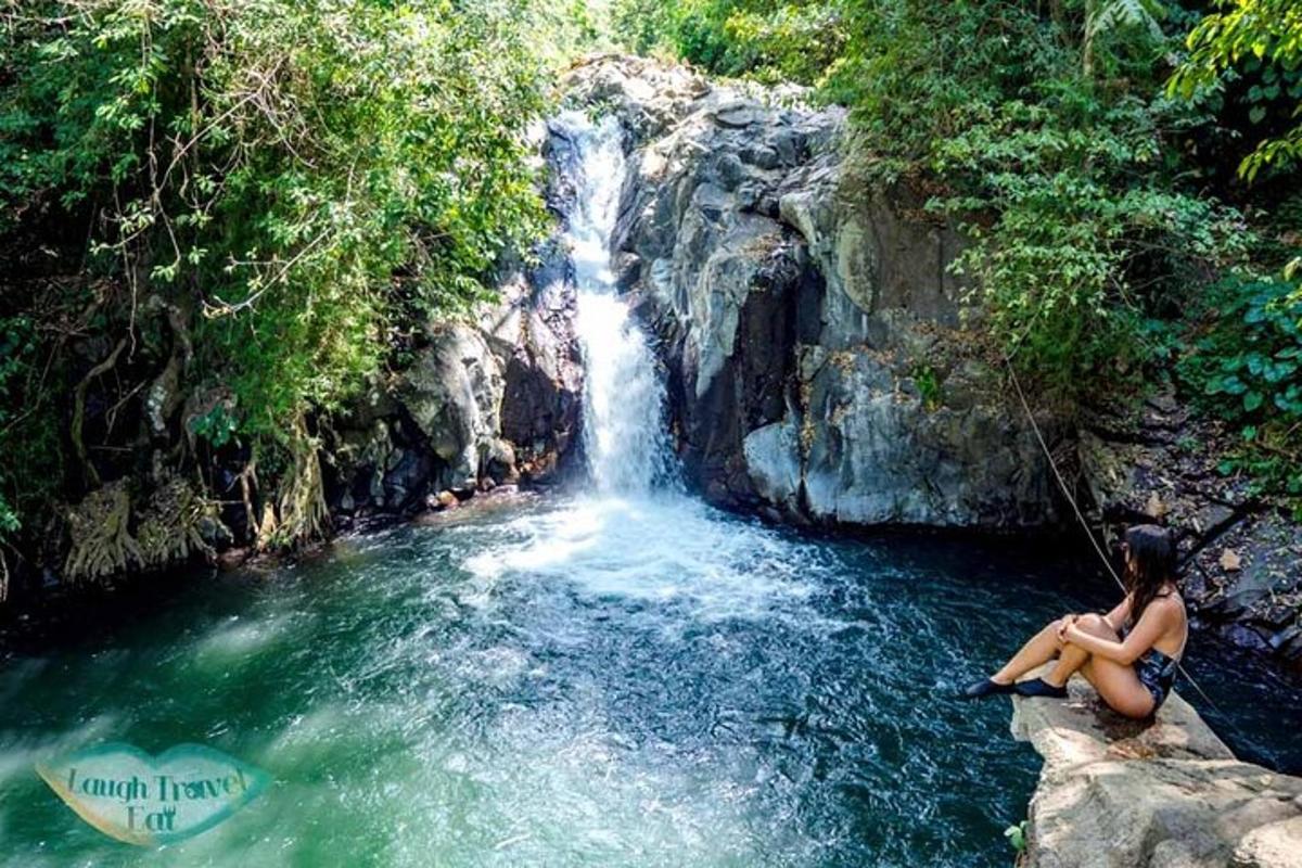 uma mulher sentada em uma rocha em frente a uma cachoeira