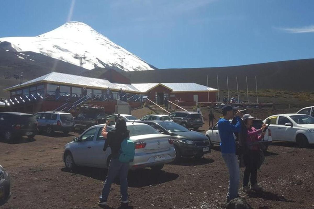 a group of people standing around a parking lot with a snow covered mountain