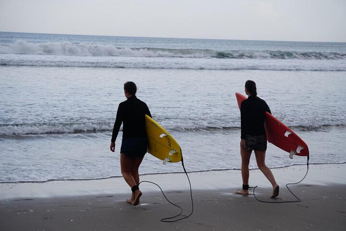dua orang berjalan di pantai dengan papan selancar mereka