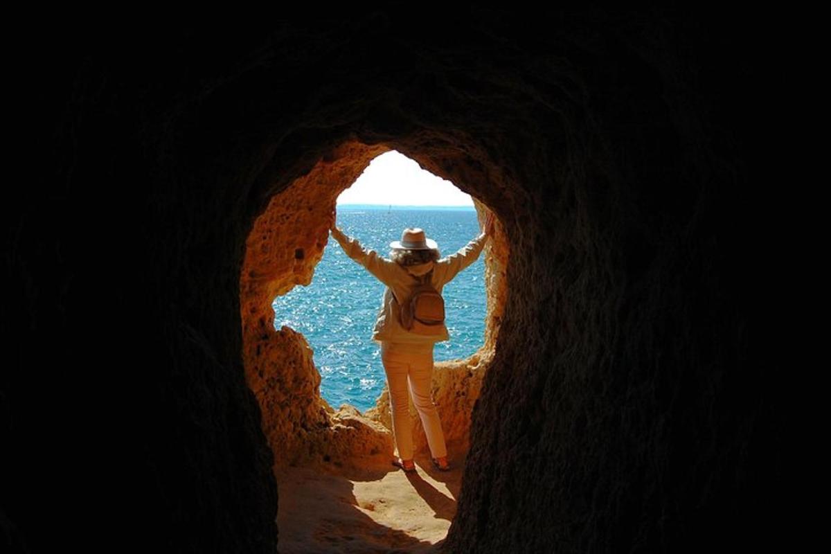 Una mujer parada en una cueva mirando el océano.