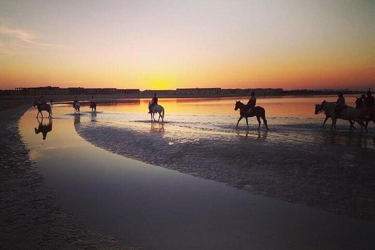 Un grupo de personas montando a caballo en la playa al atardecer.