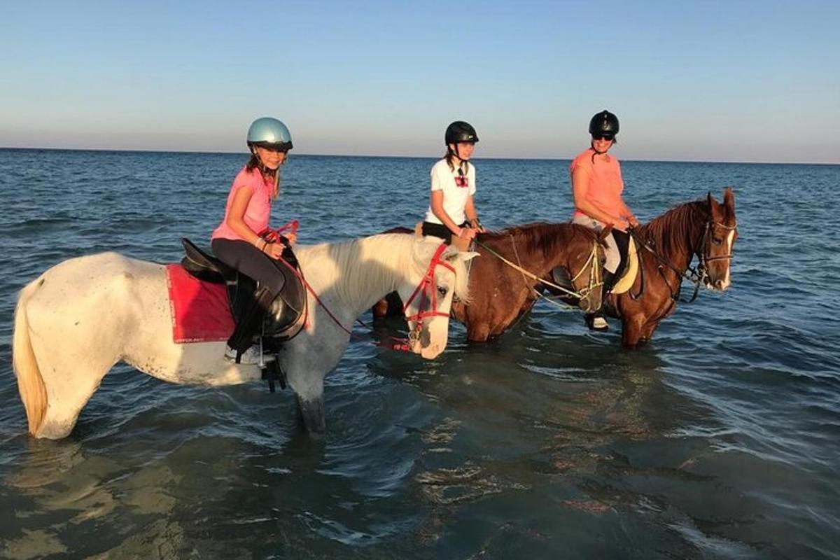 tres persones munten a cavall a l'aigua