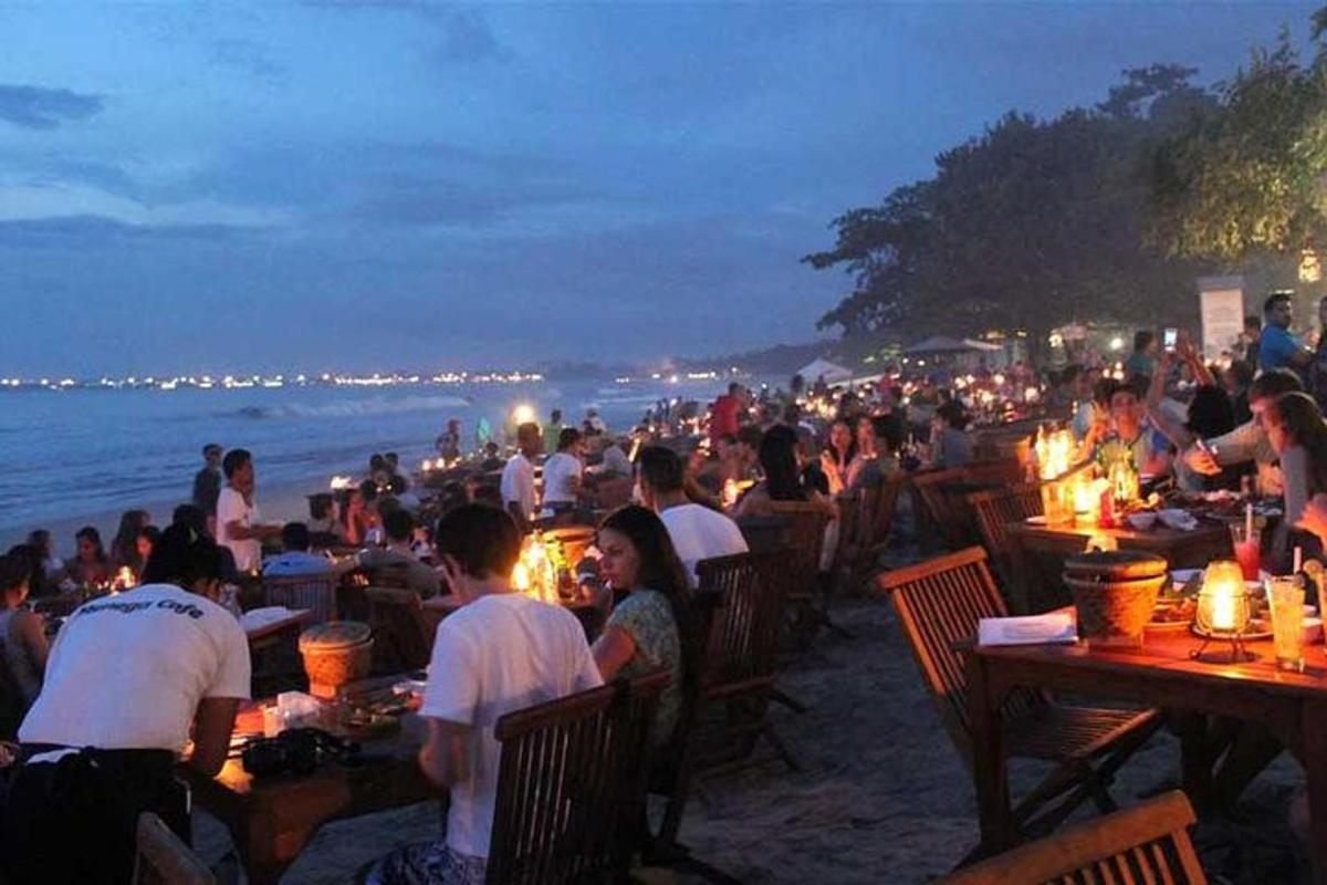 sekelompok orang yang duduk di meja di pantai pada malam hari