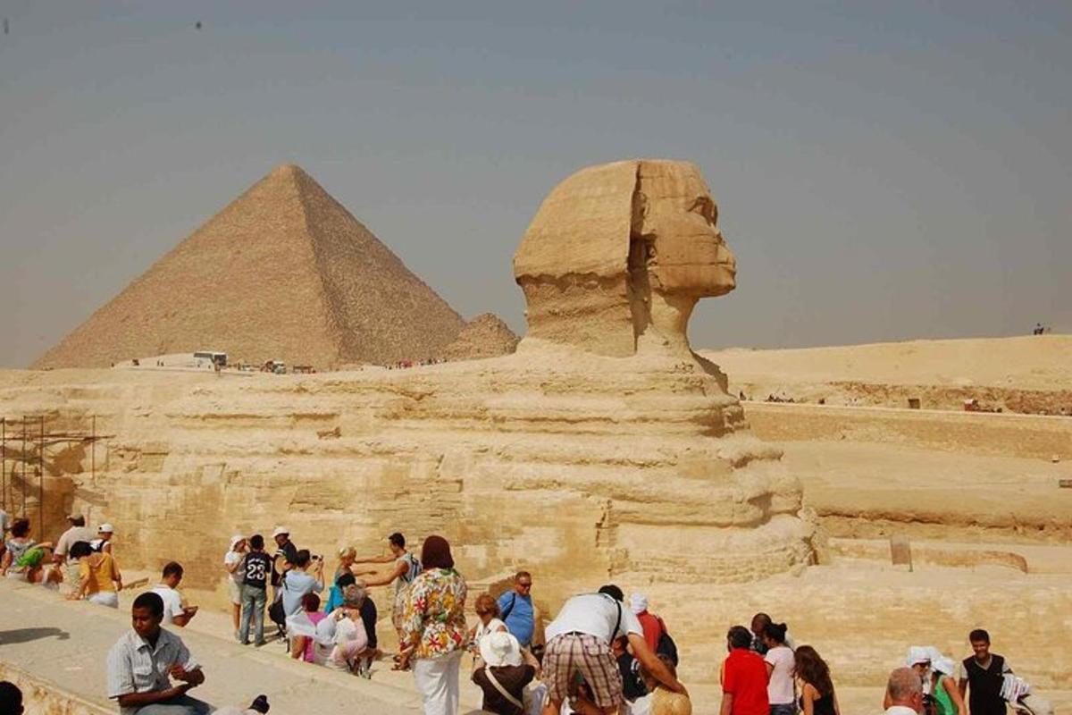 en gruppe mennesker, der står omkring en statue foran pyramiden