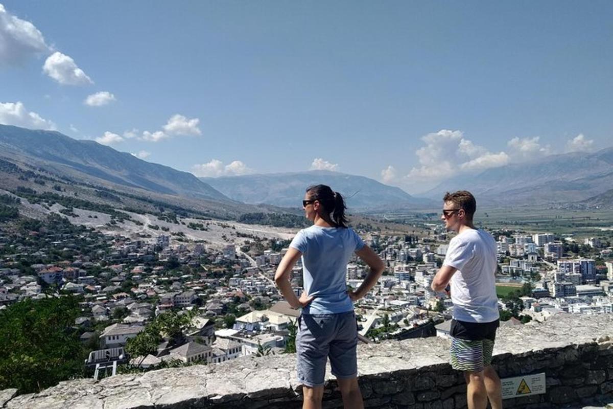 two people standing on top of a wall looking at a city