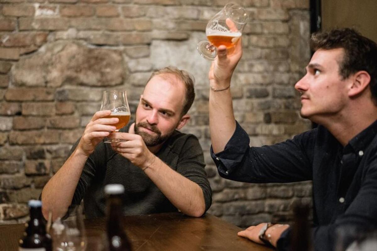 two men sitting at a table holding up glasses of beer