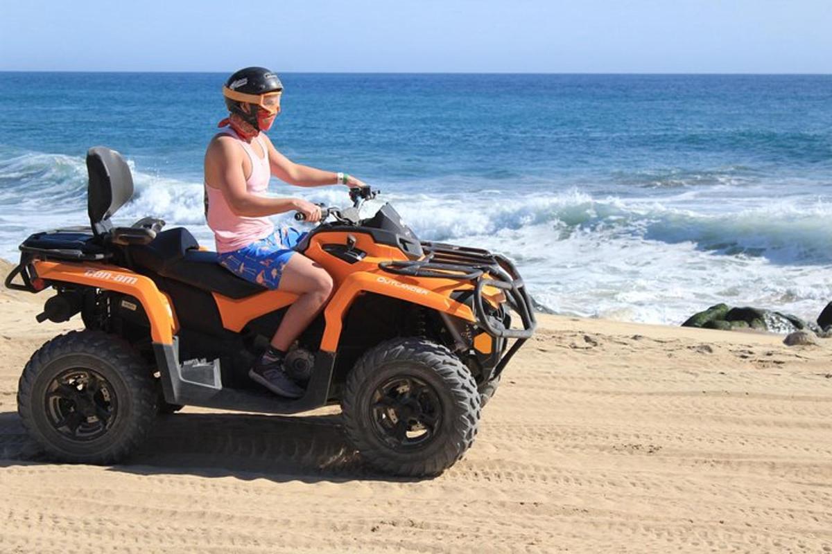 un uomo che guida un quad arancione sulla spiaggia
