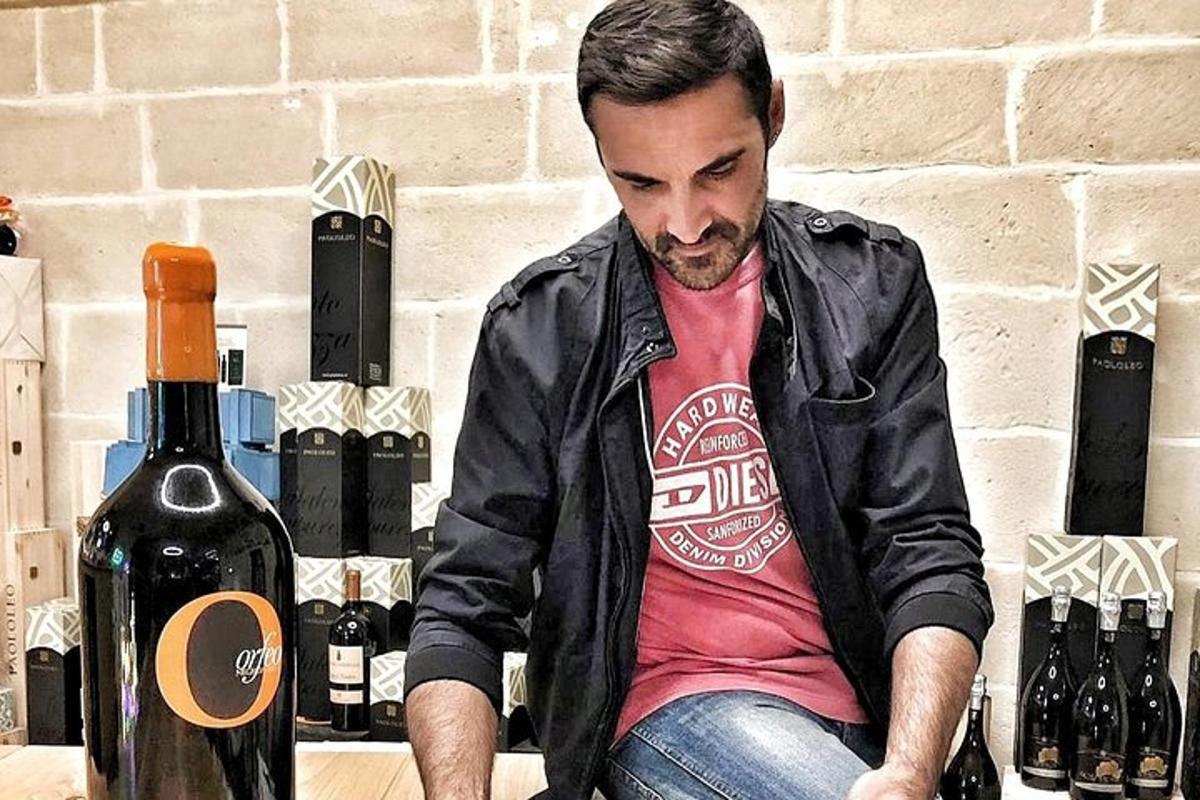 a man in a leather jacket sitting next to a bottle of wine