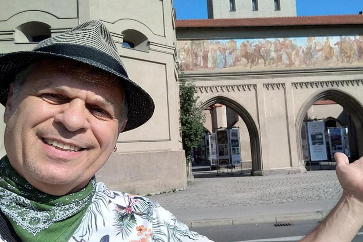 Un bărbat cu pălărie zâmbește în fața unei clădiri