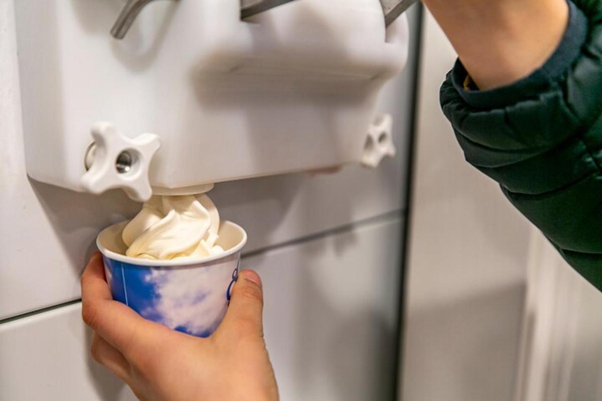 una persona che tiene in mano una tazza di panna montata in un distributore
