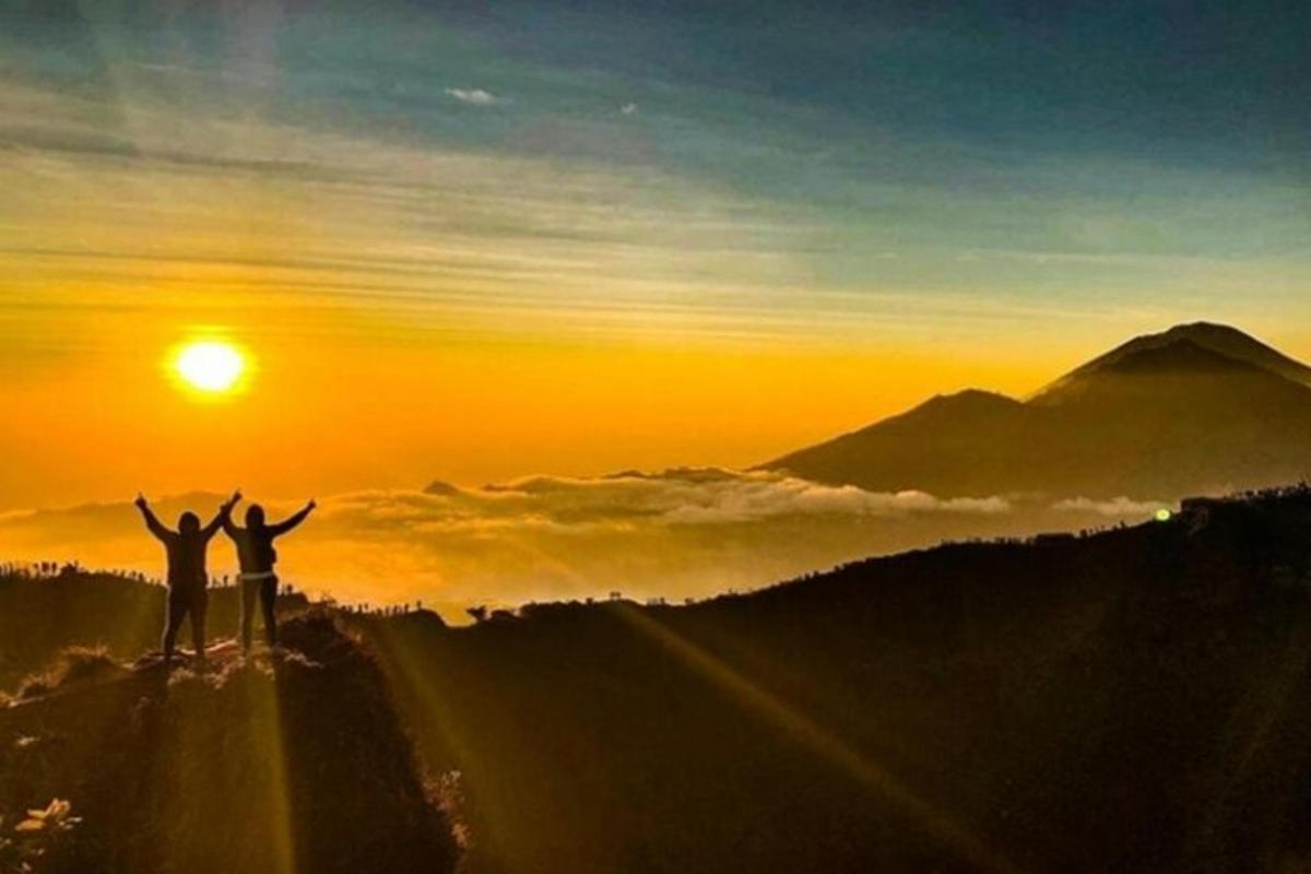 Dos personas de pie en la cima de una montaña al atardecer