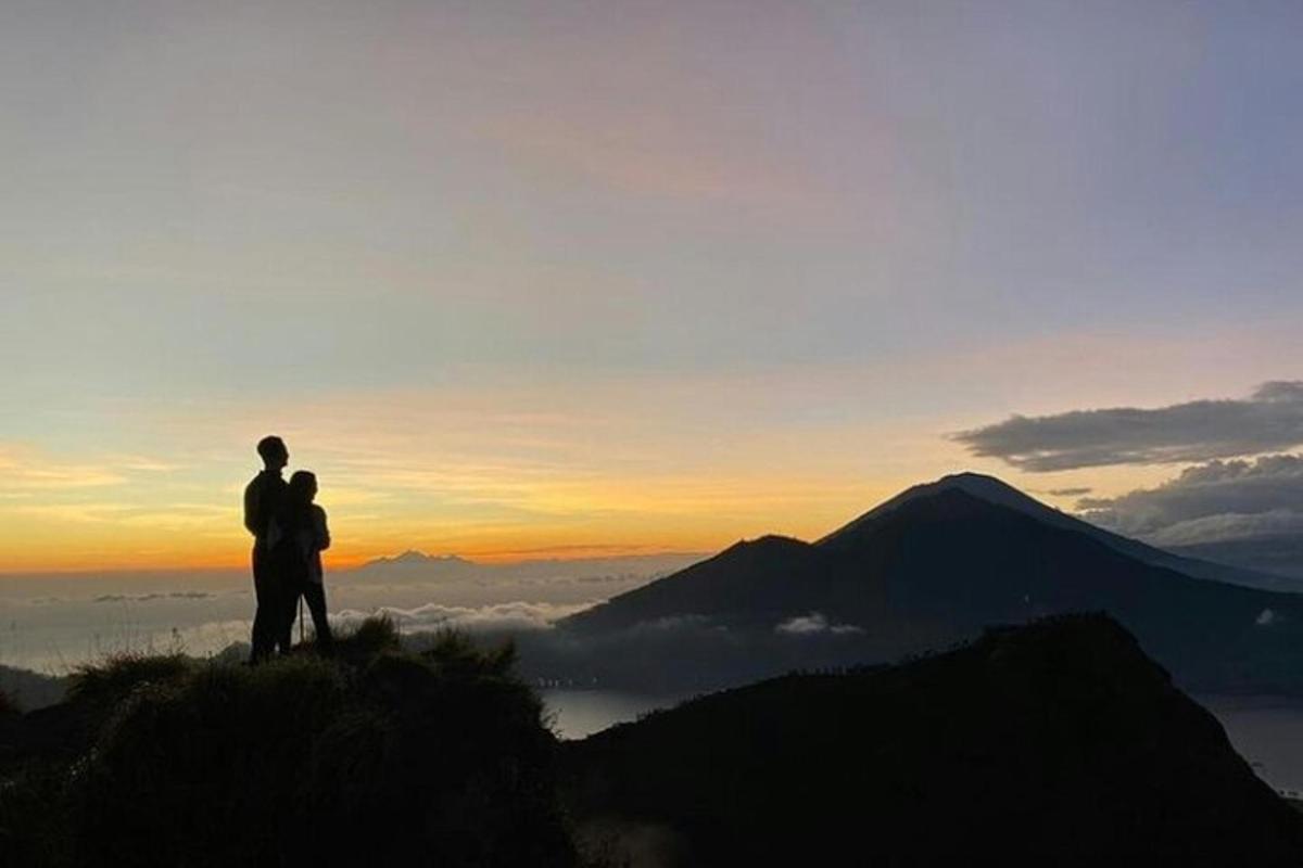 a couple standing on top of a mountain at sunset