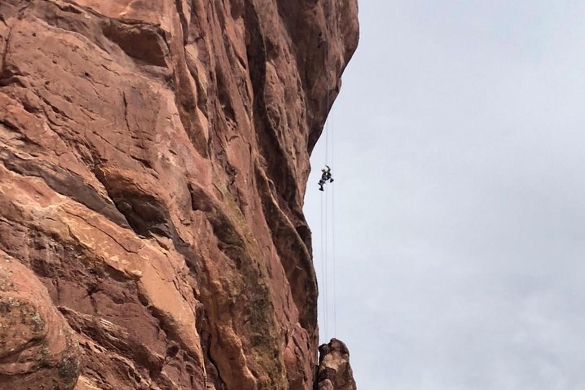 una persona che si cala in corda doppia da una parete rocciosa