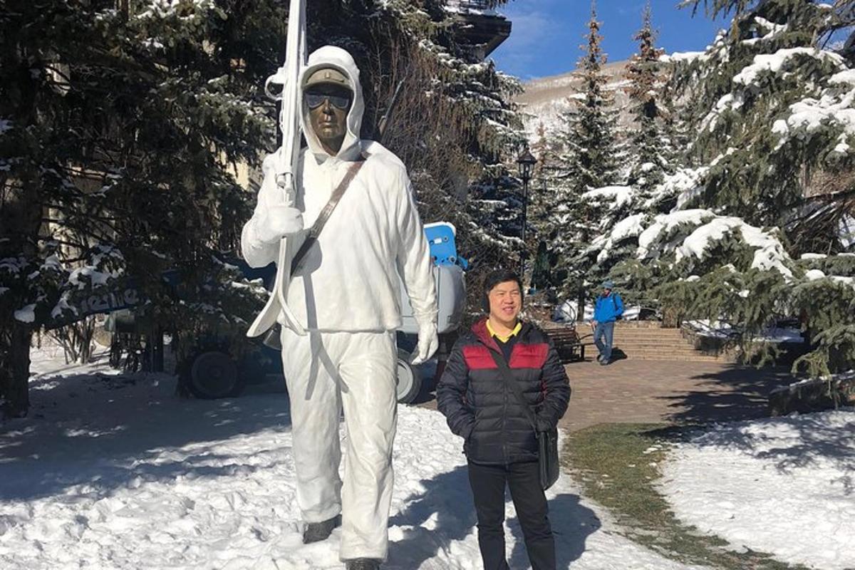 Un hombre de pie junto a una estatua de un hombre sosteniendo esquís.