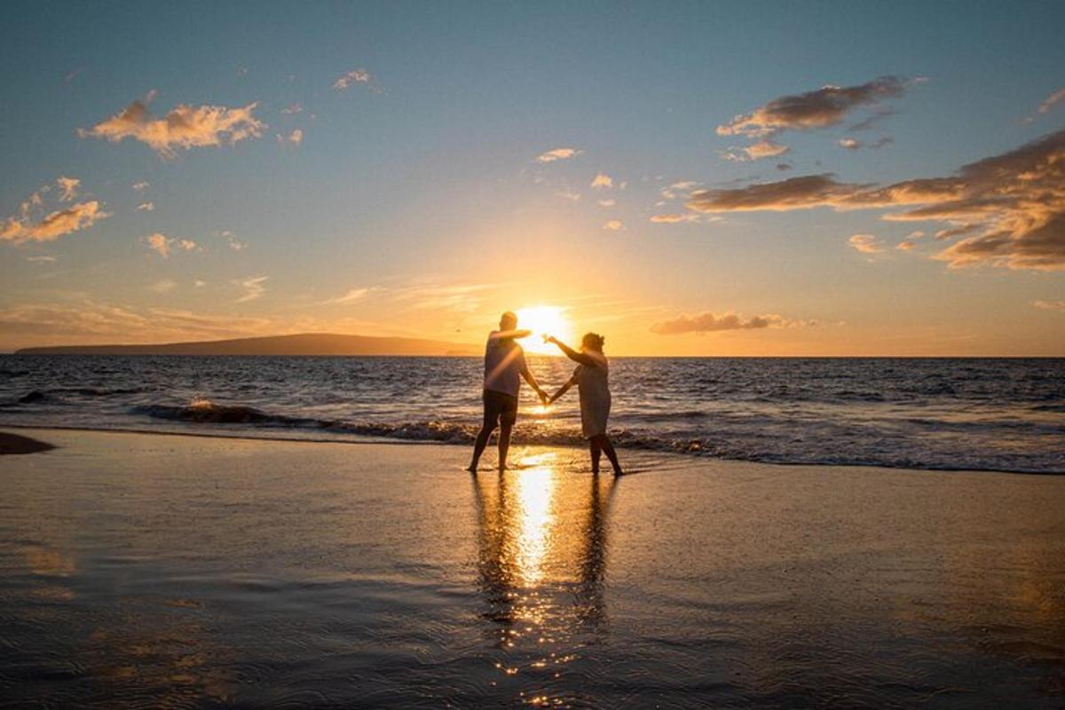dva človeka, ki se sprehajata po plaži ob sončnem zahodu