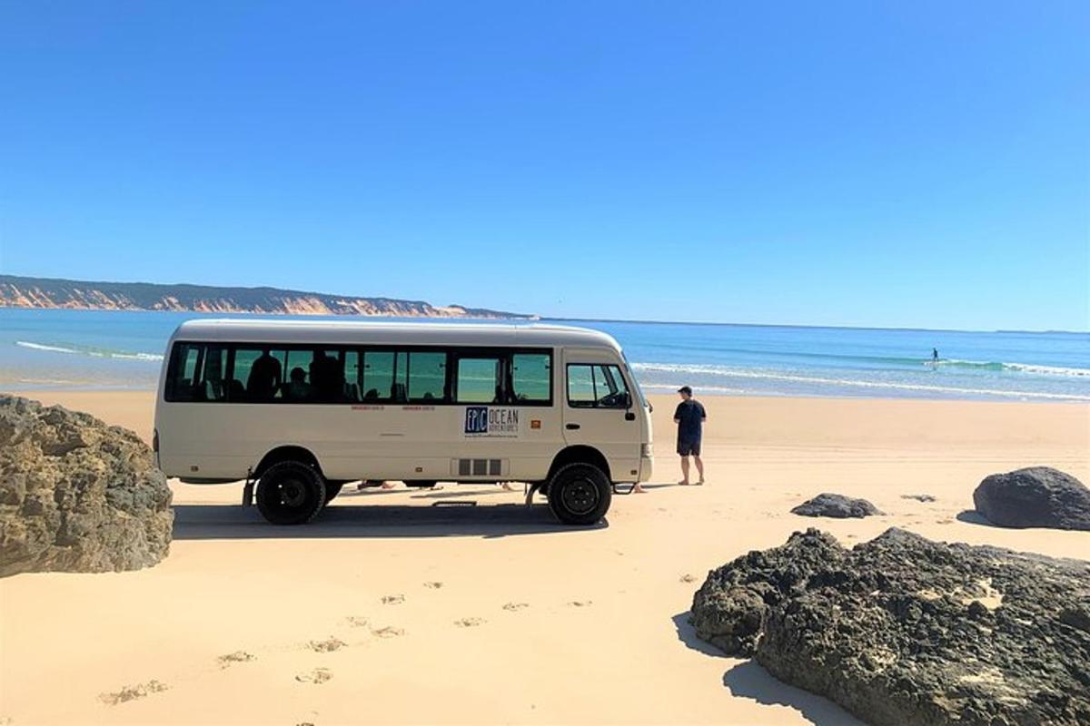 a white bus parked on the beach with a man