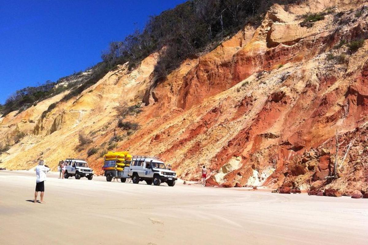 a man standing on a beach next to two trucks