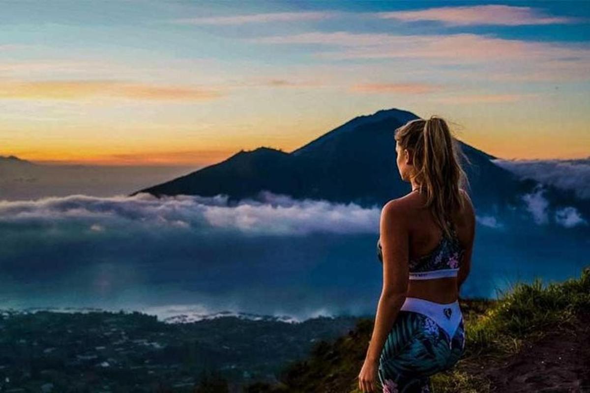 Una mujer parada en la cima de una montaña mirando la puesta de sol