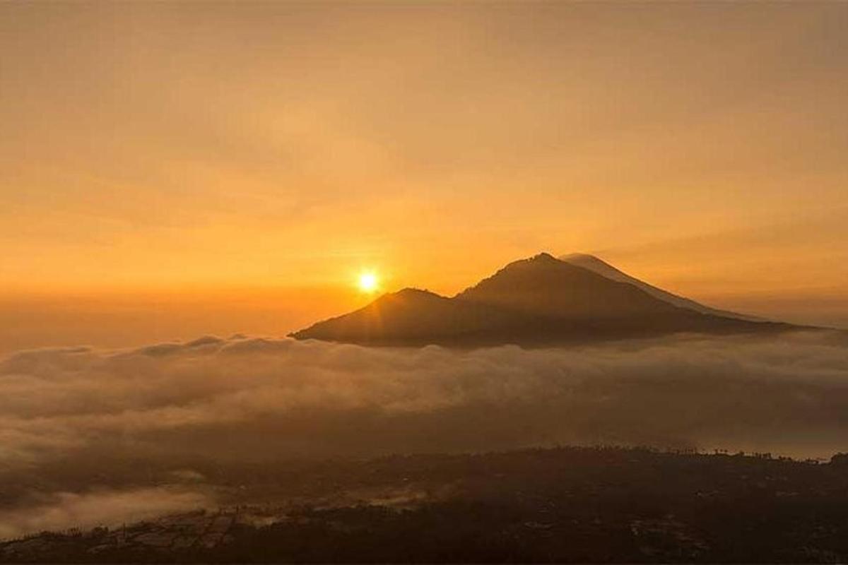 a mountain rising above a layer of fog at sunset