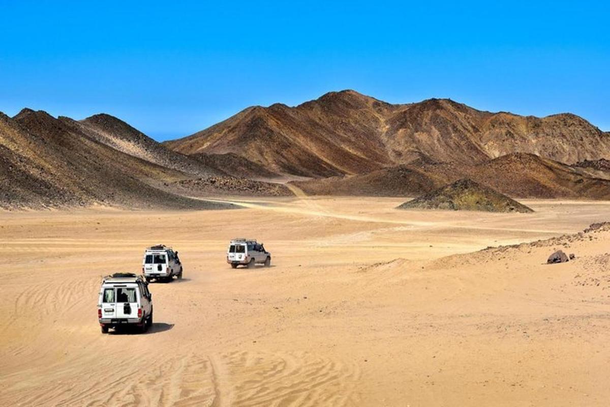 três veículos estacionados em um deserto com montanhas ao fundo