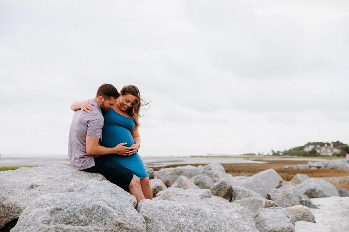 a man and a pregnant woman sitting on rocks at the beach