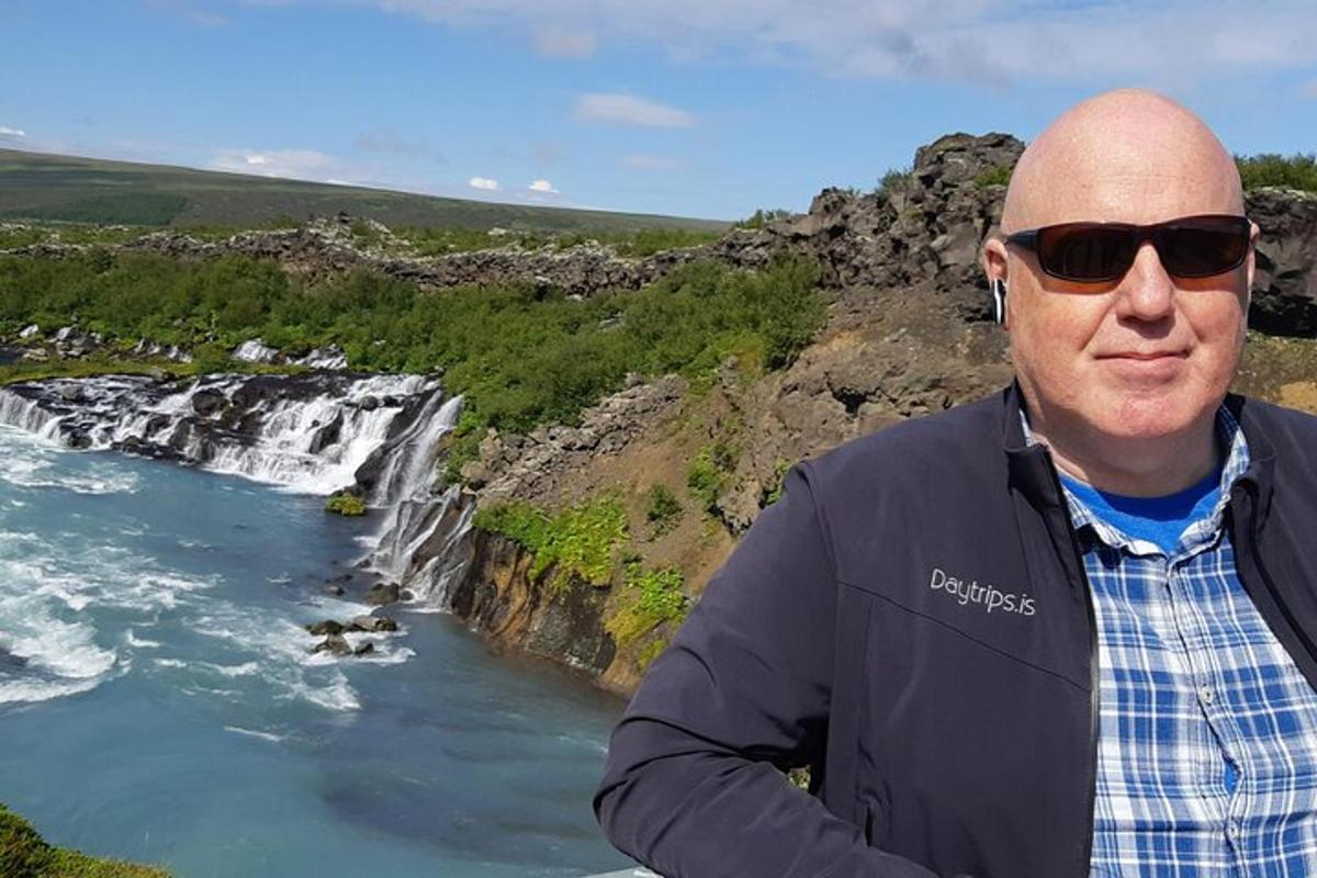 Maður með sólgleraugu stendur fyrir framan foss