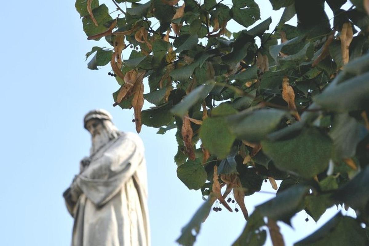 uma estátua em pé ao lado de uma árvore com folhas