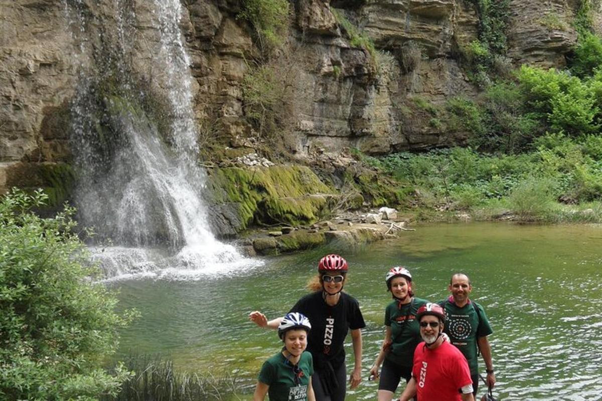 um grupo de pessoas em pé em um rio em frente a uma cachoeira