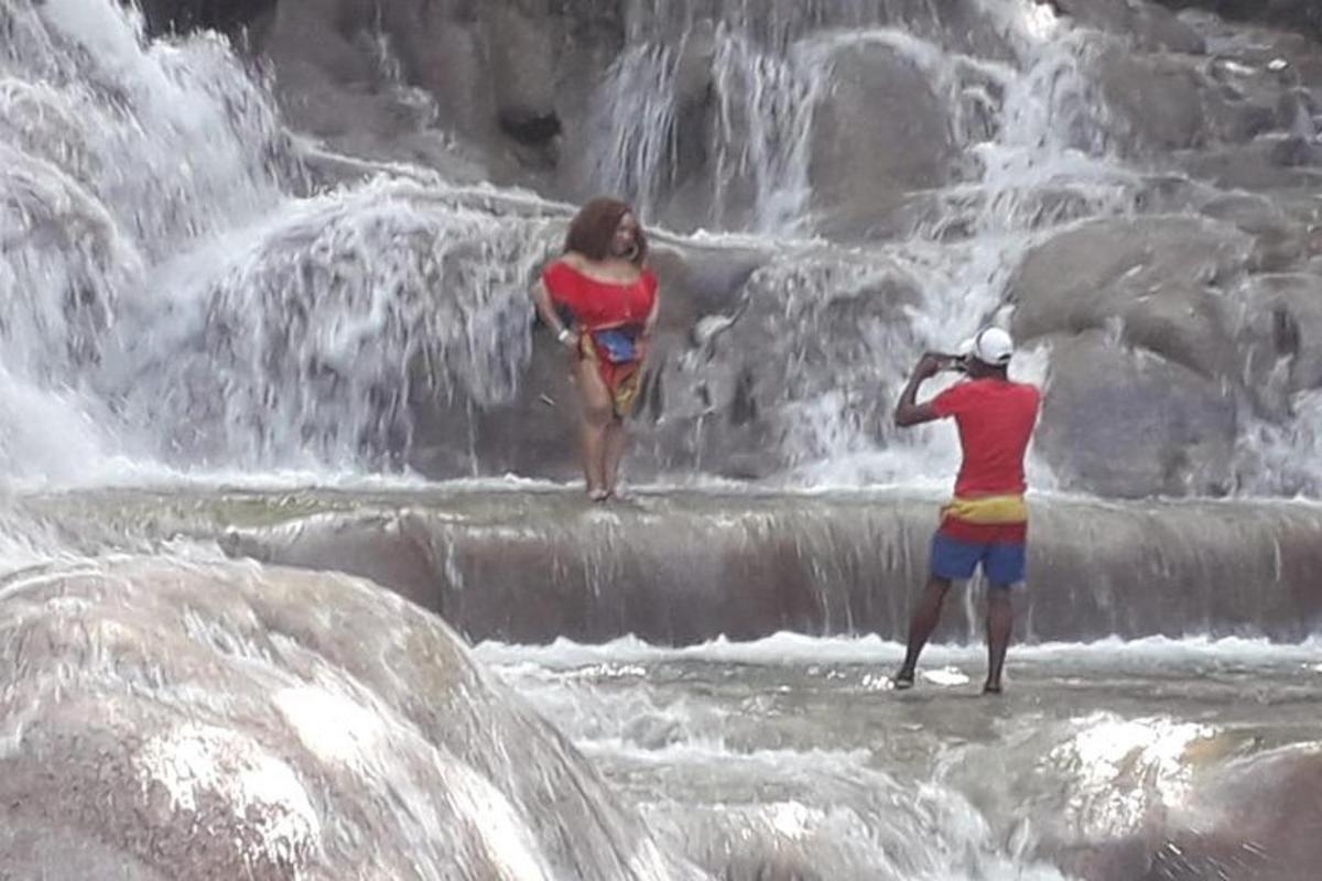 two people standing in the water near a waterfall