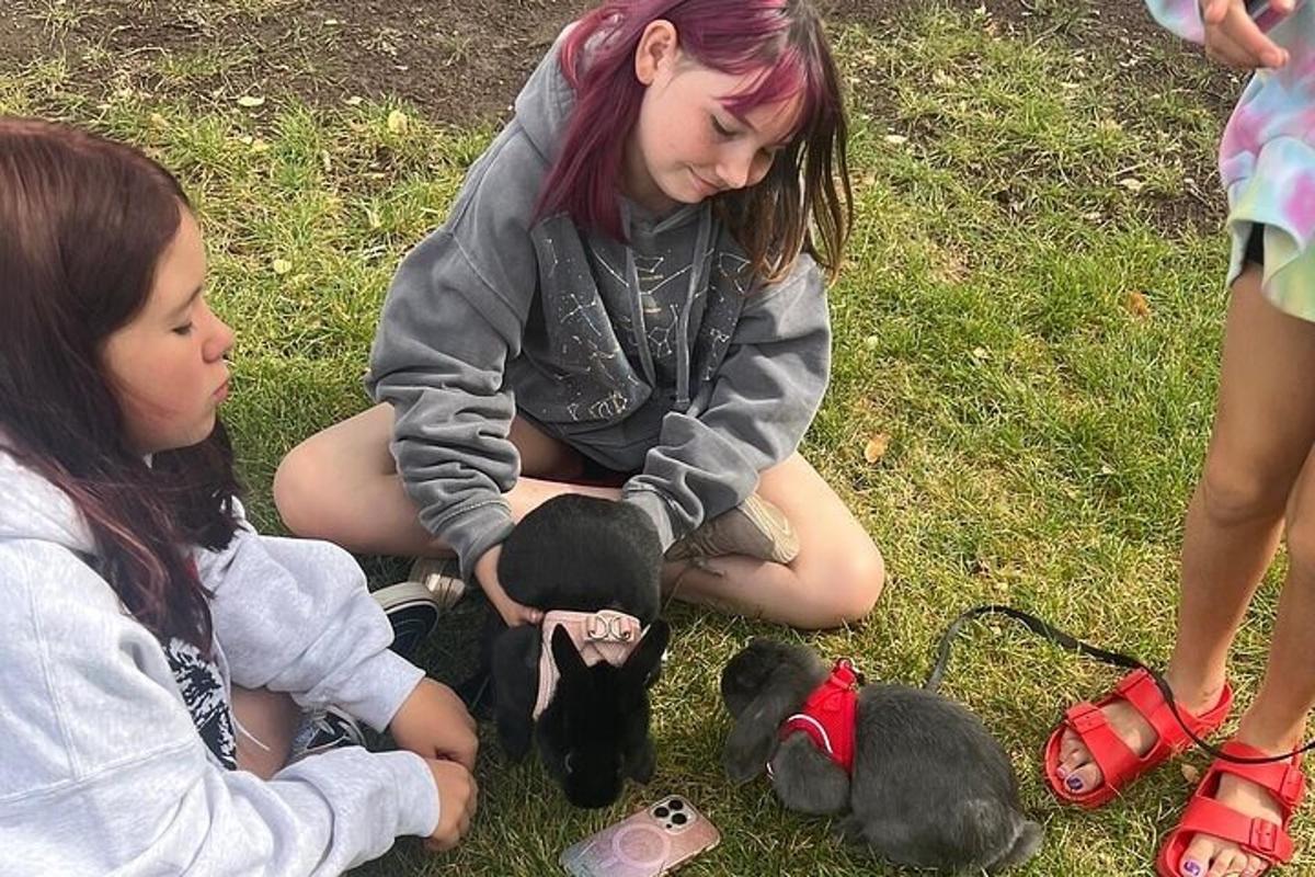 two girls sitting on the grass playing with a stuffed animal