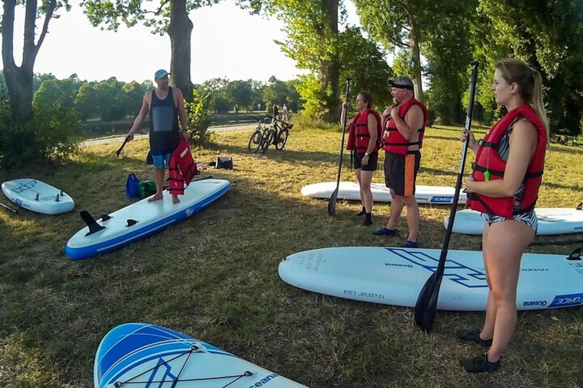 skupina lidí stojících v trávě s paddleboardy