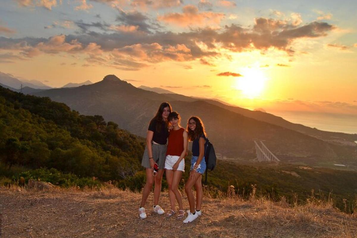 three girls standing on top of a mountain at sunset