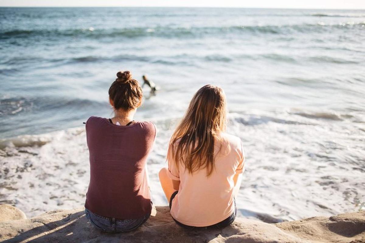 two women sitting on the beach looking at the ocean
