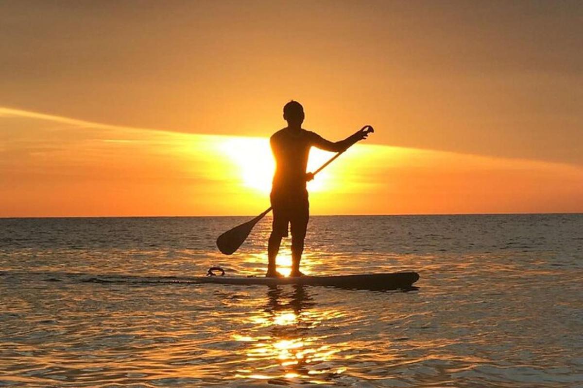 Un hombre de pie sobre una tabla de remo en el océano al atardecer