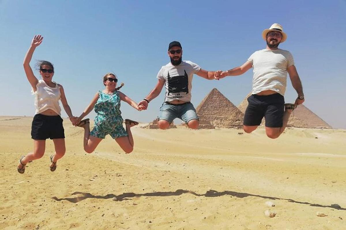 tři lidé skákají do písku před pyramidami