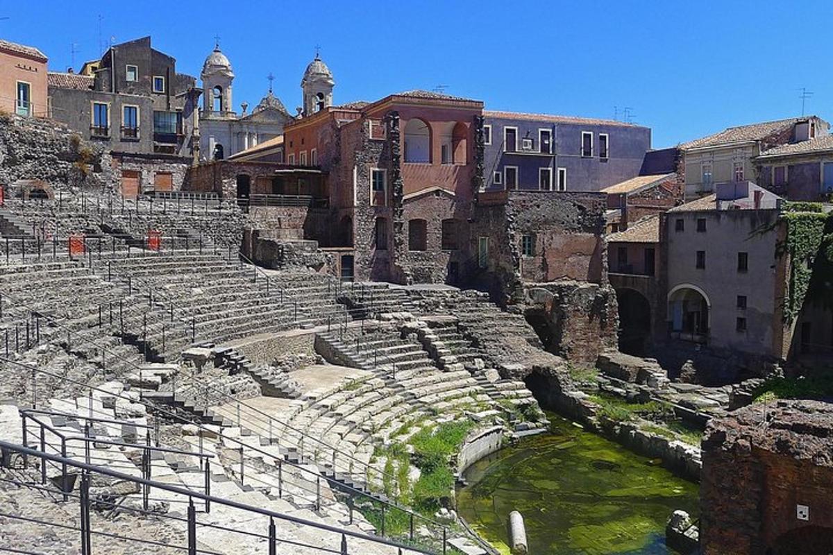 an ancient amphitheater in a city with water and buildings