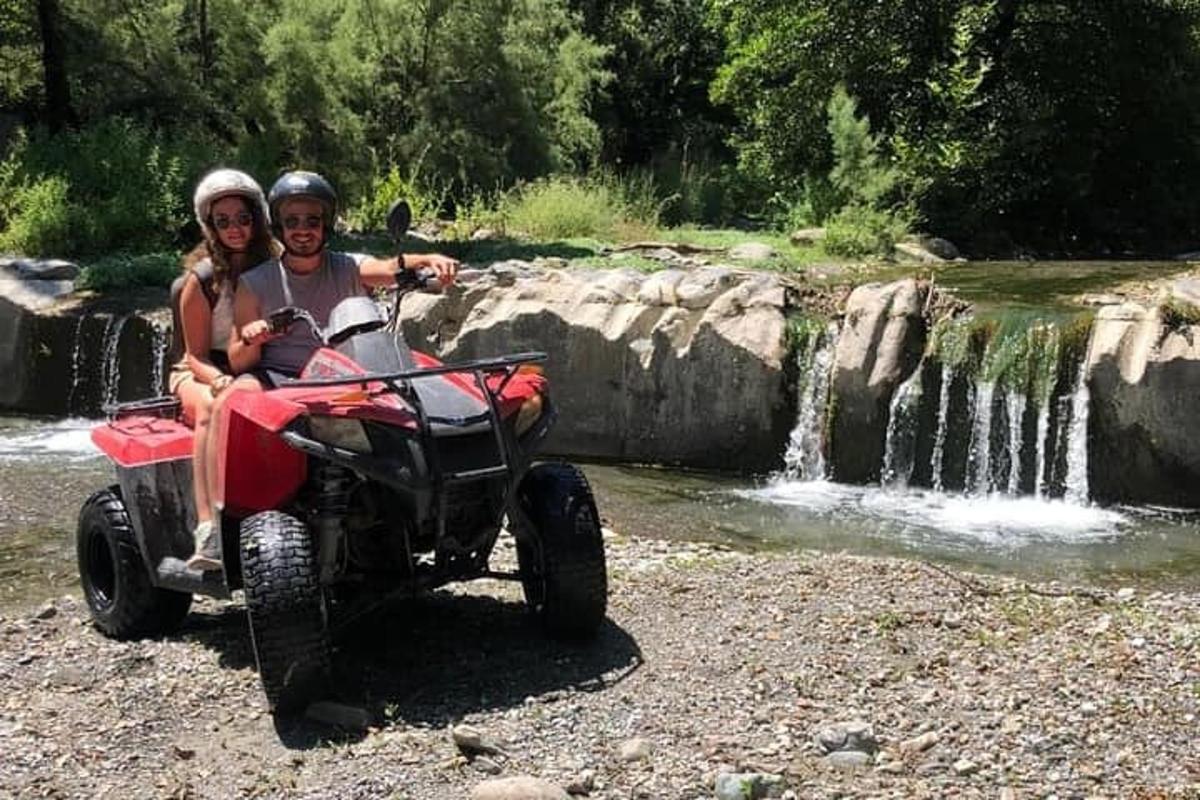 vīrietis un sieviete uz kvadracikla ūdenskrituma priekšā