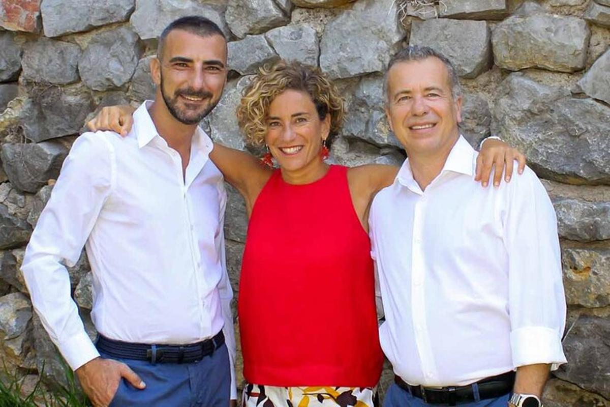 Két férfi és egy nő áll egy kőfal mellett