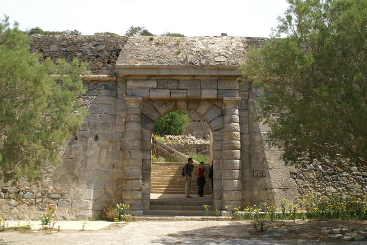 duas pessoas caminhando através de um arco em uma parede de pedra