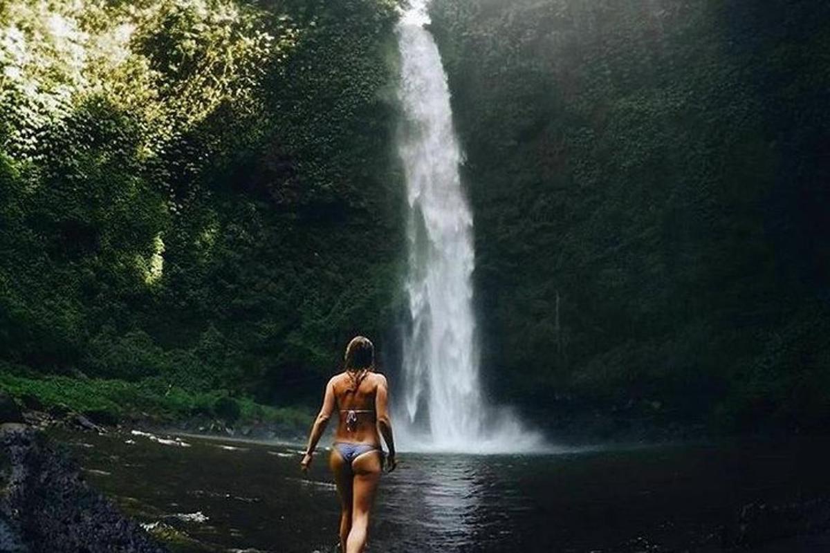 uma mulher caminhando na água em frente a uma cachoeira