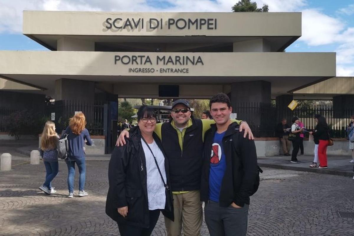 trijų žmonių grupė, stovinti priešais pastatą