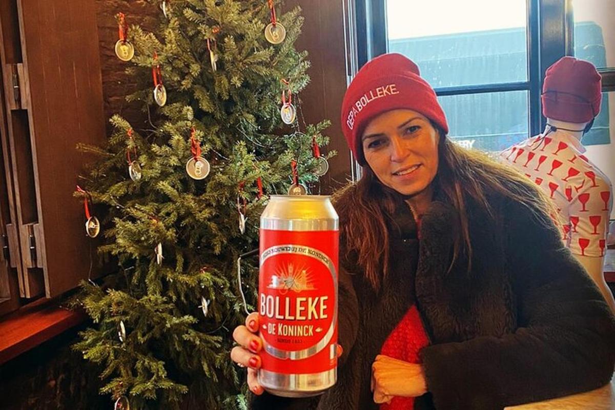 una donna che tiene in mano una lattina di birra calda davanti a un albero di Natale
