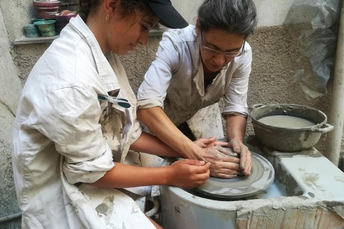 two people making a pot on a pottery wheel