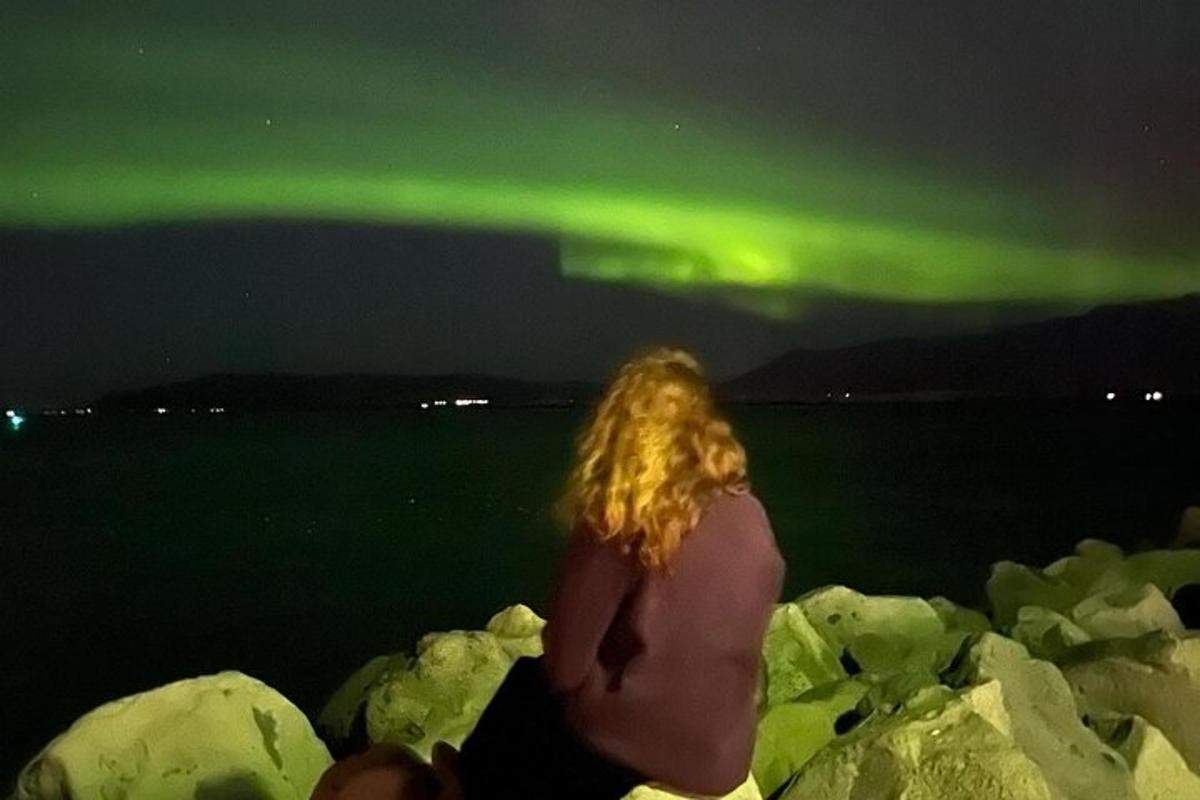 una donna seduta sulle rocce che osserva l'aurora boreale