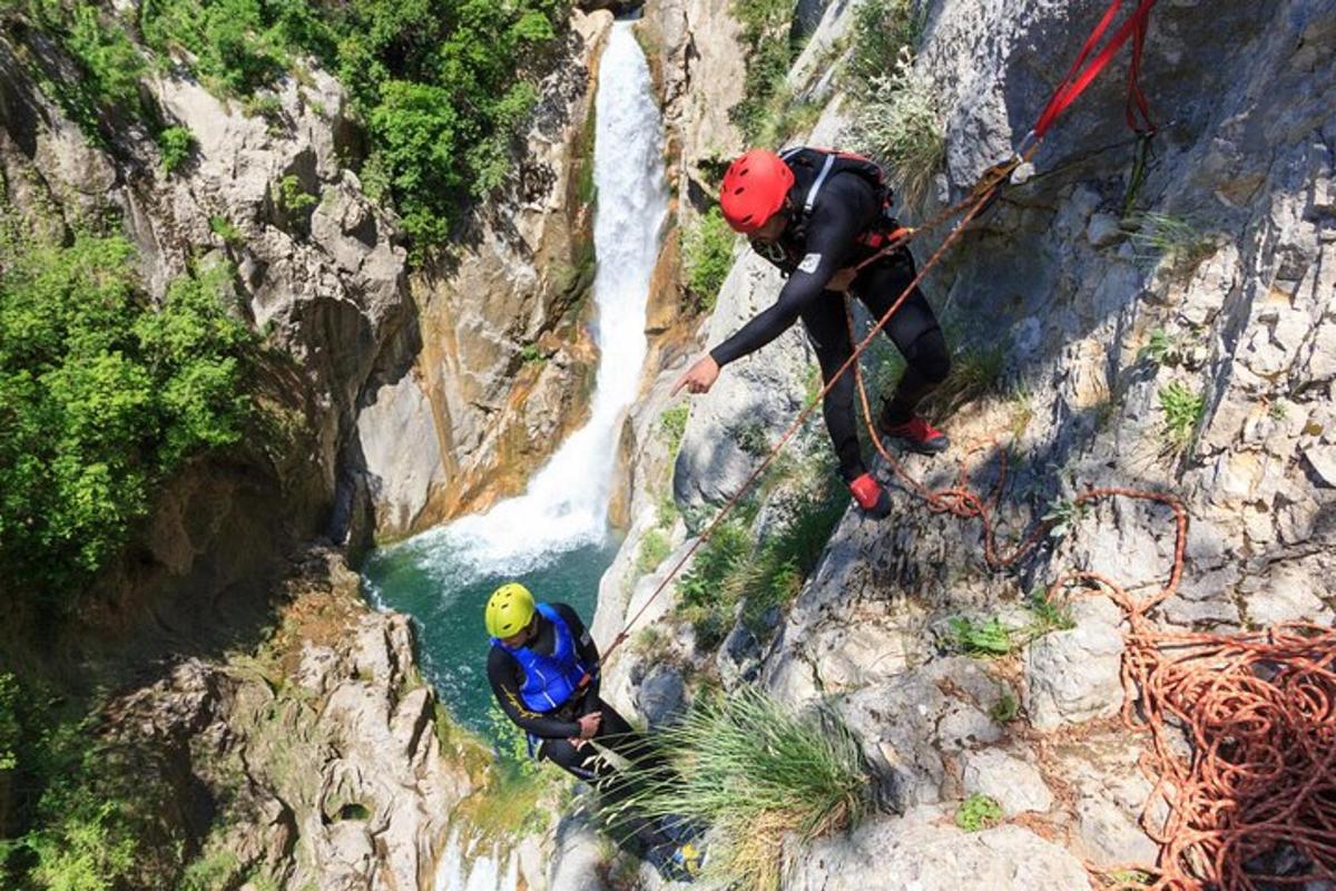 dues persones baixant en ràpel per una muntanya amb una cascada