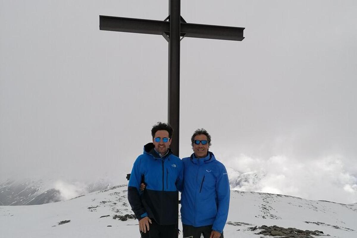 two men standing in front of a cross on a mountain