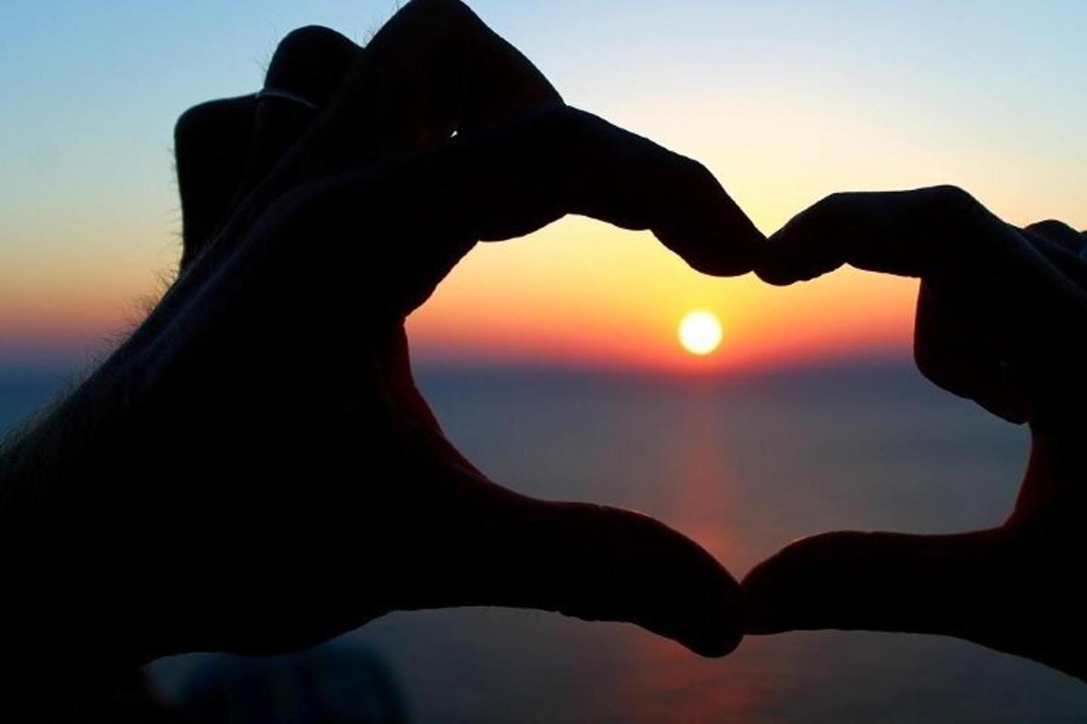 a silhouette of two people making a heart with the sunset in the background