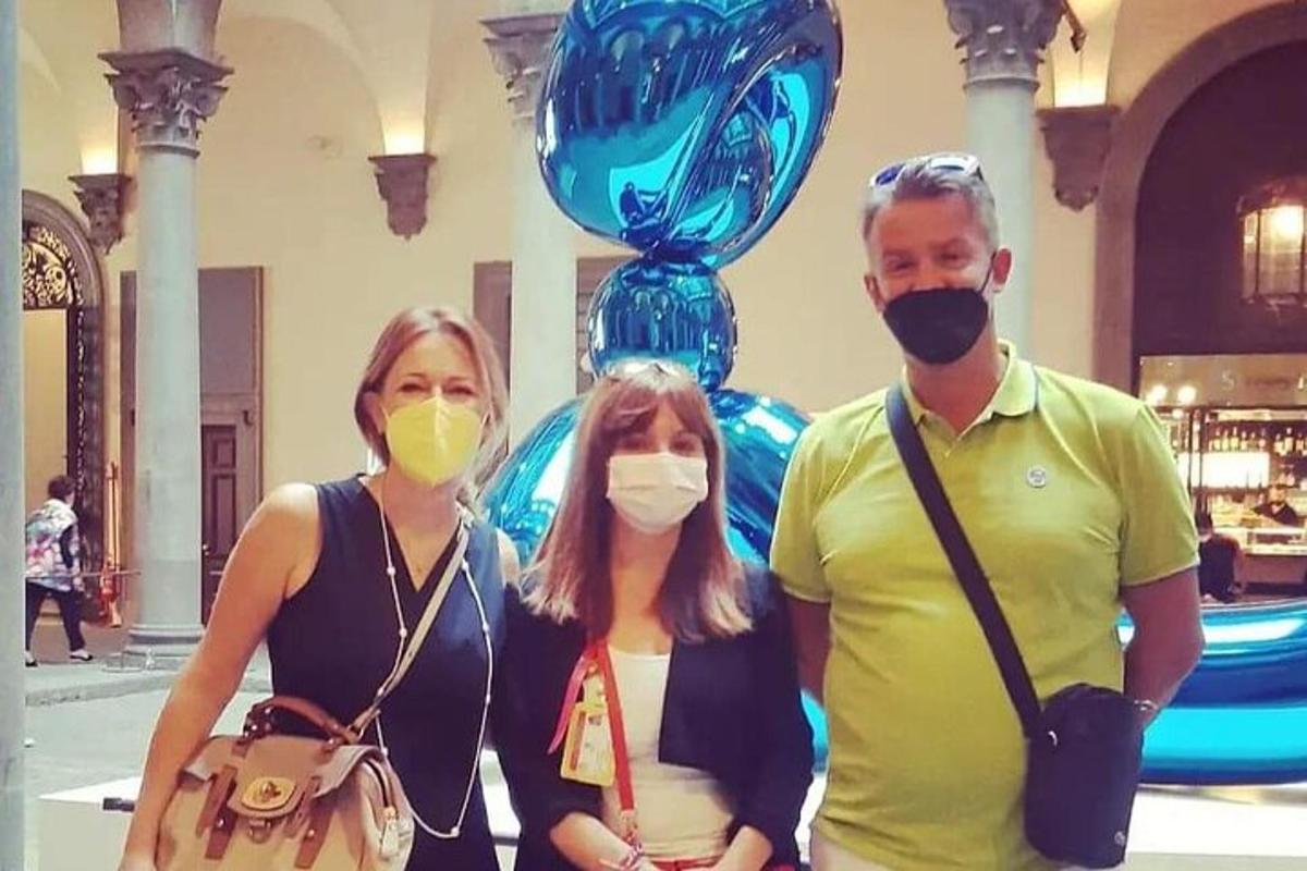 trys kaukėti žmonės stovi priešais skulptūrą