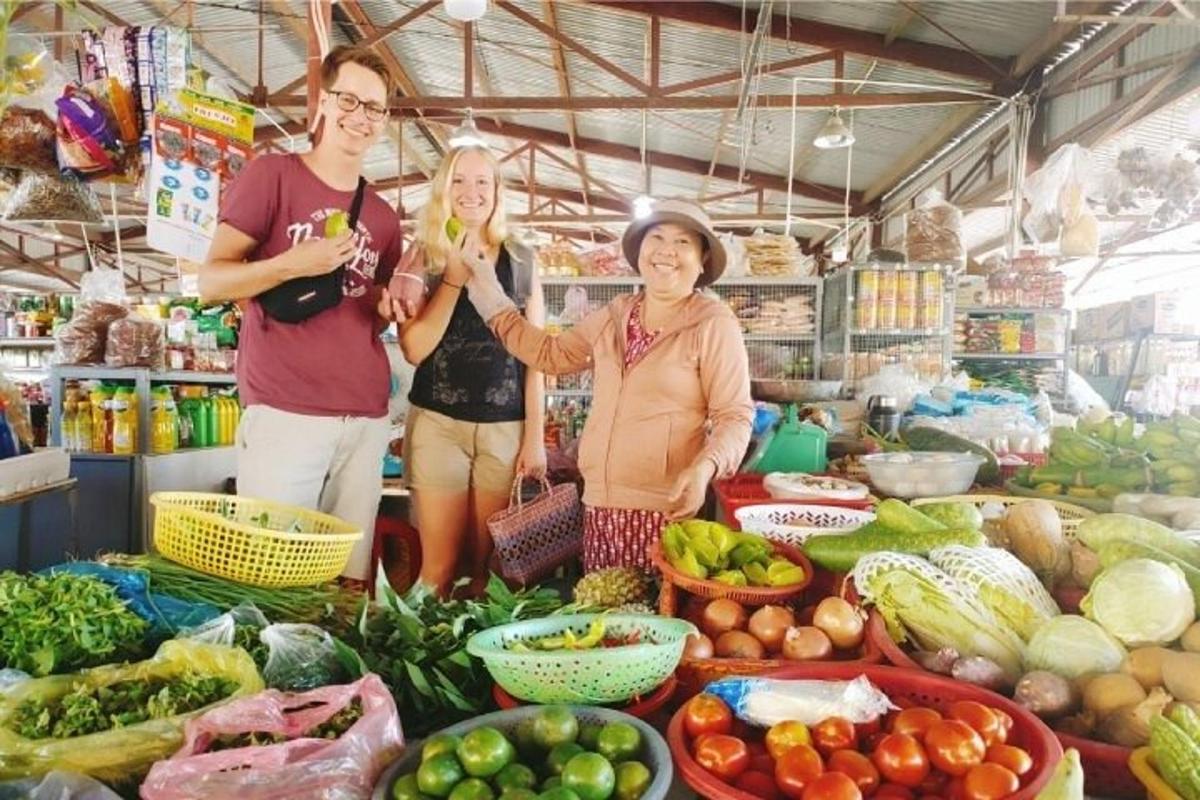 tiga orang berdiri di pasar dengan buah-buahan dan sayur-sayuran