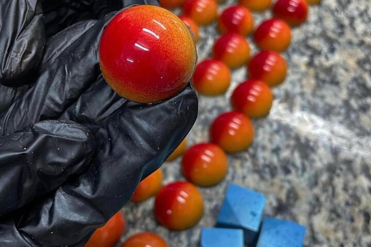 la mà d'una persona que sosté una fruita vermella al costat d'un manat de tomàquets